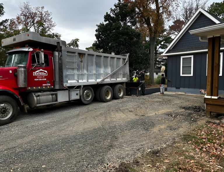 Red dump truck unloading gravel on a residential driveway for a professional paving project.