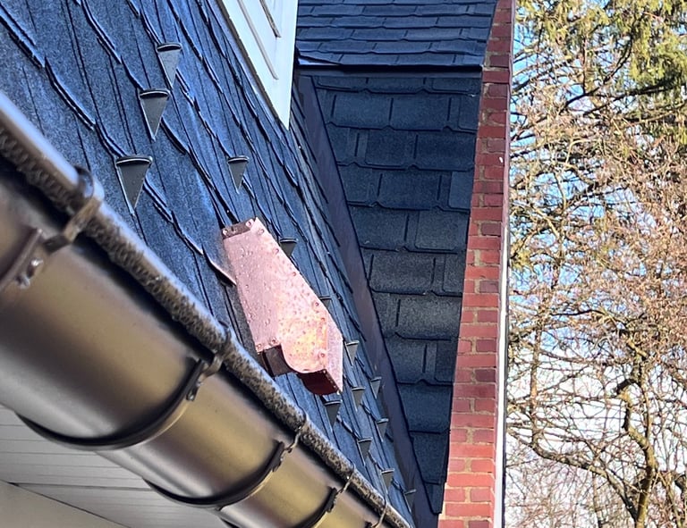 Copper flashing and snow guards installed on a steep slate shingle roof with gutters.