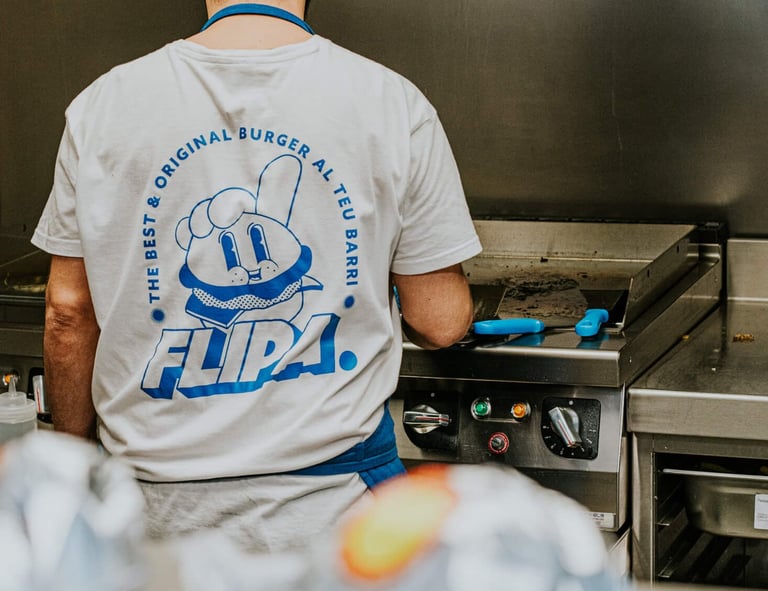 Cocinero de Flipa en cocina con camiseta de la marca mientras prepara burgers a la plancha