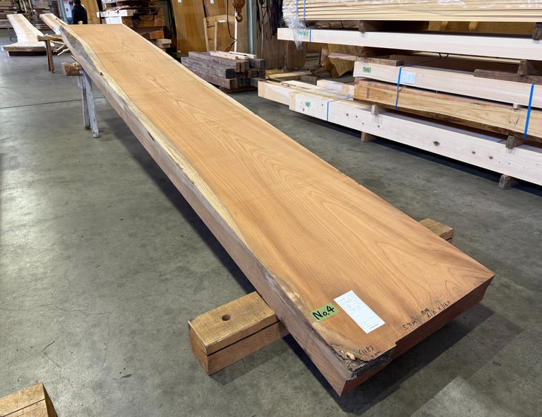 A long, single-slab live edge wood board with natural grain resting on blocks in a lumber warehouse.