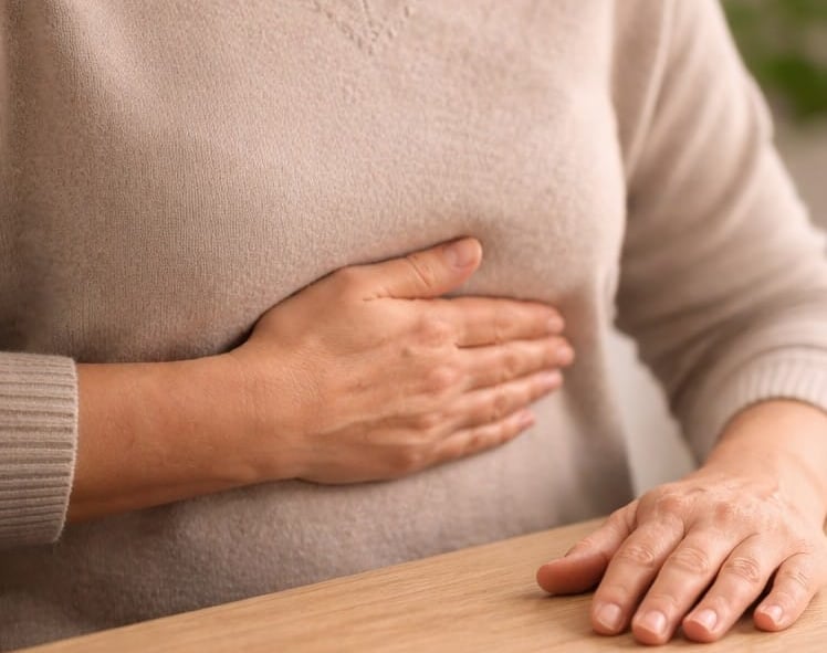 A woman holding her hand to her chest while experiencing breathing exercises at a wooden desk.