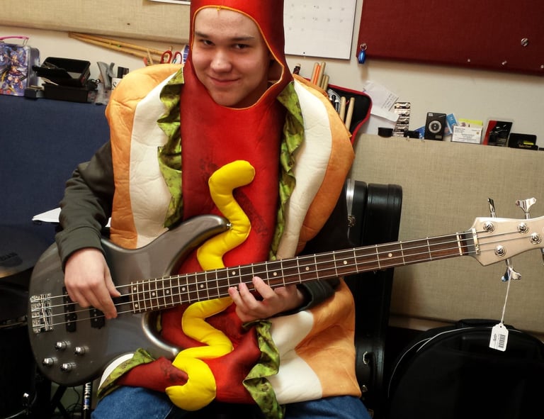 Young man in a hot dog costume learning to play the bass guitar