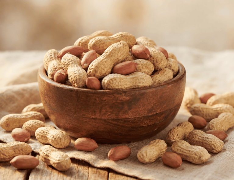 A wooden bowl filled with whole roasted peanuts in shells and shelled red skin peanuts on a rustic cloth.