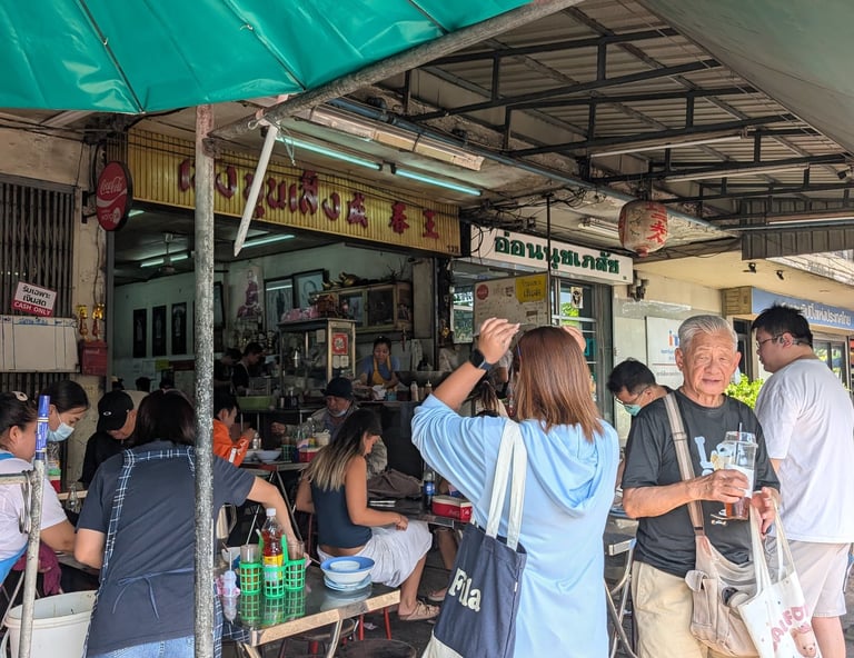 Diners eat at a busy authentic Thai street food stall under a green umbrella in Bangkok.