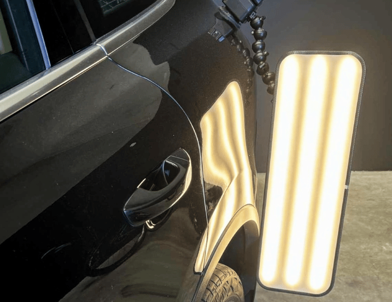 Professional paintless dent repair light board illuminating a black car for surface inspection.