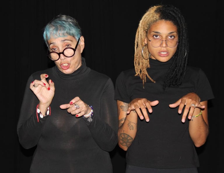 Dos mujeres actrices migrantes con camisas negras y gafas actuan como posando para la foto