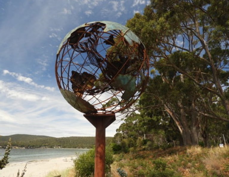 Verdigris metal globe sculpture on the beach with a mother whale and her calf in the middle of it