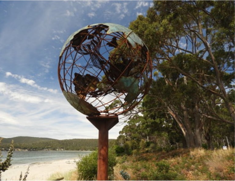 Verdigris metal globe sculpture on the beach with a mother whale and her calf in the middle of it