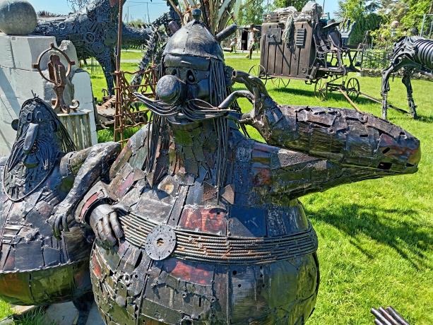 Whimsical scrap metal sculpture of cartoon character Obelix in an outdoor art garden.