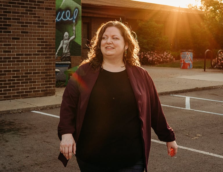 Smiling woman walking in a brick building parking lot at sunset with golden hour lighting.