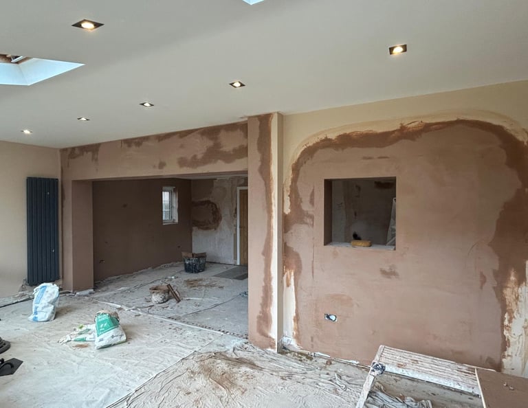 Freshly applied brown plaster on interior walls during a home renovation project with recessed lighting.