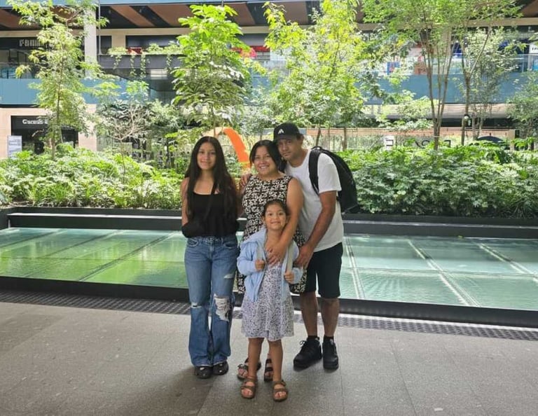 A family of four poses together in a modern outdoor shopping mall with lush green plants.