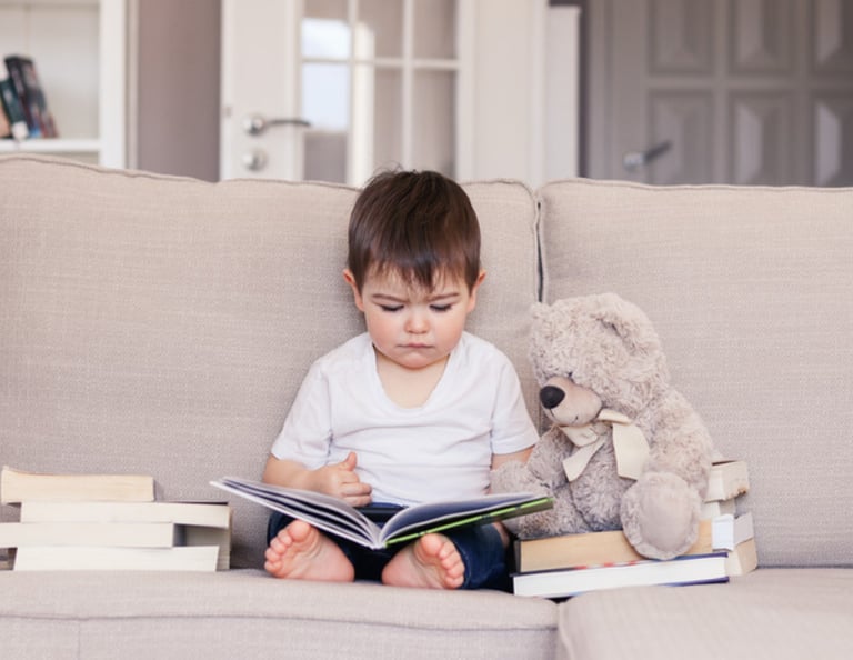 un petit garçon assis sur un canapé qui lit un livre avec un ours en peluche