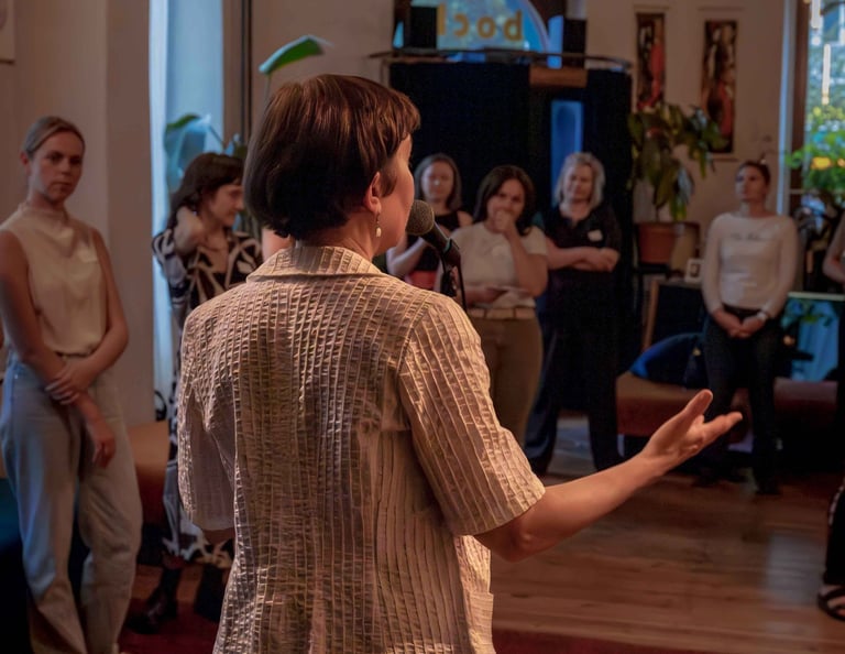 Female public speaking trainer behind microphone, talking to women during workshop.