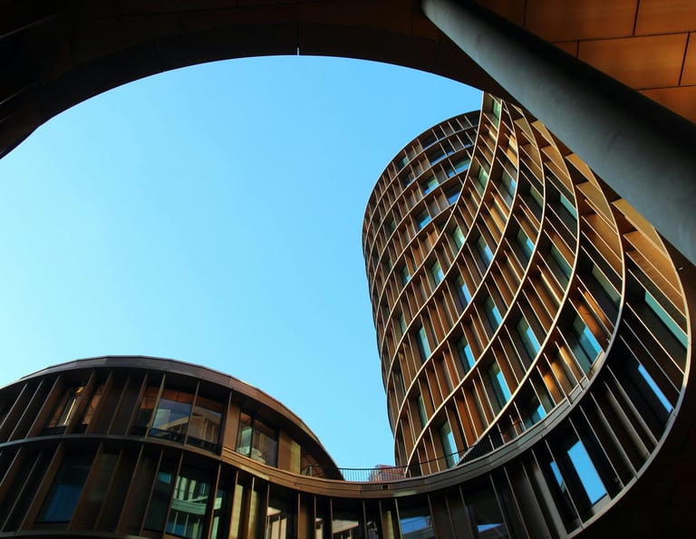 Vista inferior de edifícios contemporâneos com formas curvas, estruturas metálicas e céu azul.