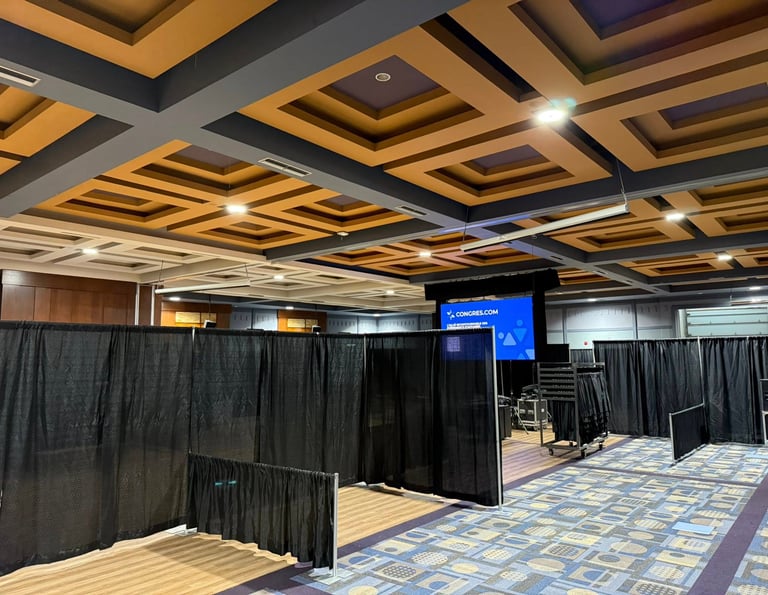 Spacious ballroom conference venue with black pipe and drape partitions and coffered ceiling.