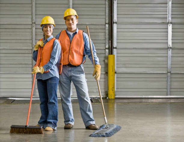 a man and woman in safety vests and hard hats cleaning warehouse