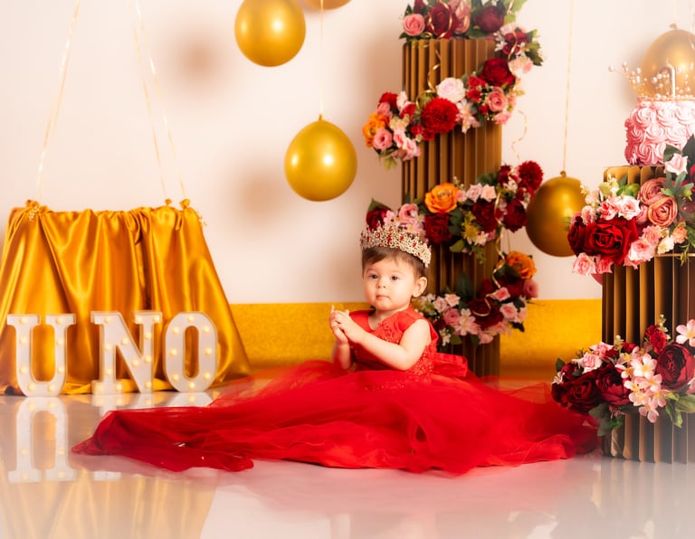 a baby girl in a red dress sitting on a floor