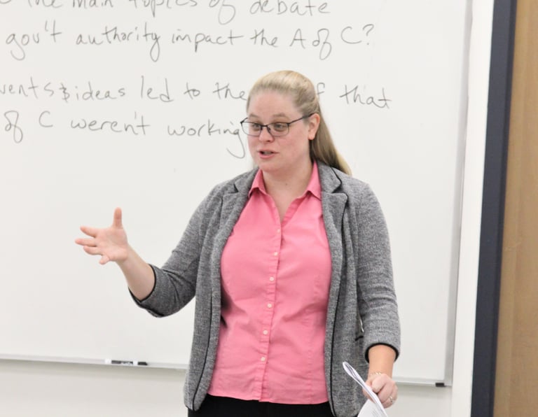 Dr. Hooton in front of a white board at the front of a classroom, teaching.