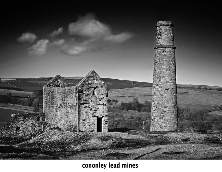 a black and white photo of a chimney and the ruins of cononley lead mines