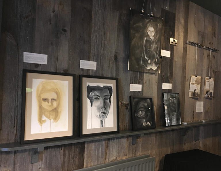 wood panelled wall with art works on the wall and shelf. Dark colours. White labels.