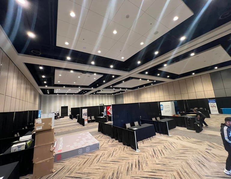 Professional trade show floor setup in a modern conference hall with black draped booths and event signage.