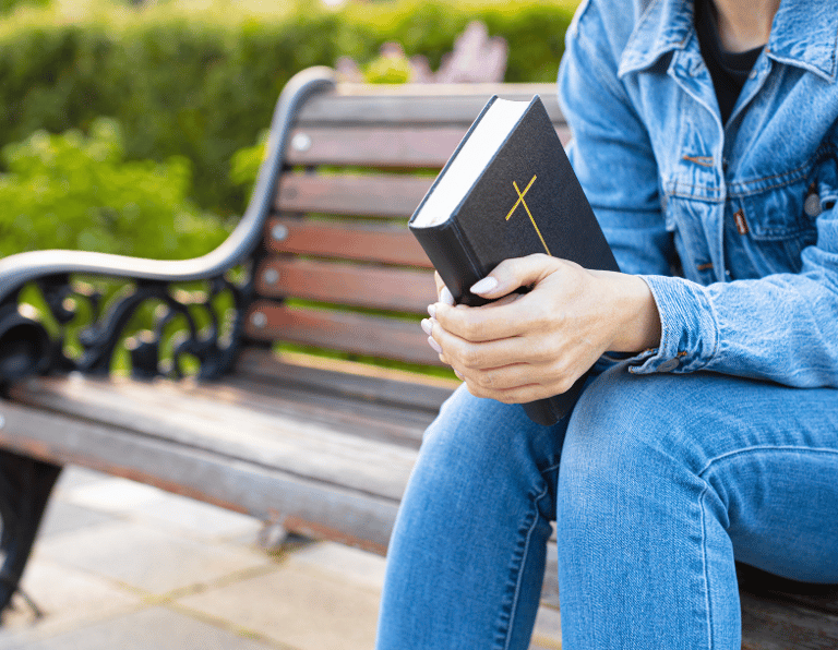 Girl sitting on a park bench holding a bible 