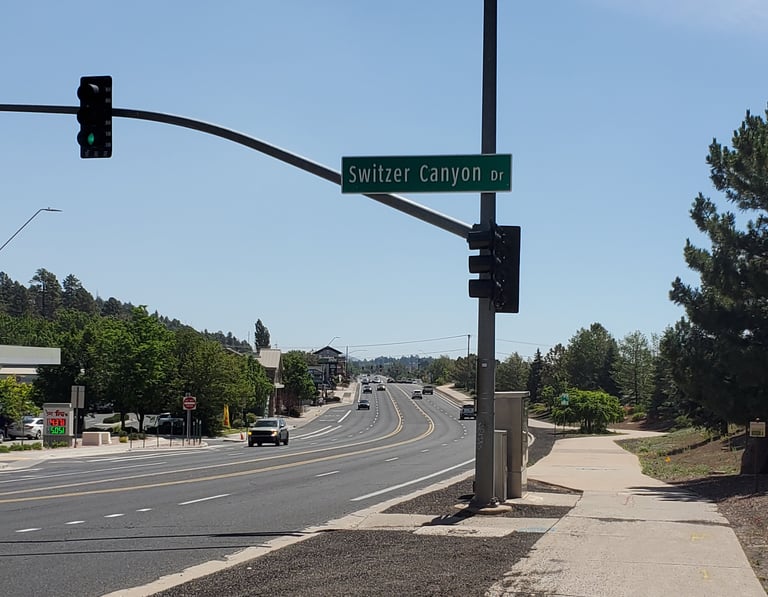 A street sign for Switzer Canyon Drive hanging over a sunny multi-lane highway in Flagstaff Arizona.