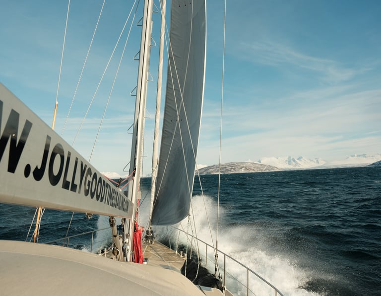 Seilbåt i fart i Lofoten, rigg og seil synlig mens sjøsprøyt slår over dekk.