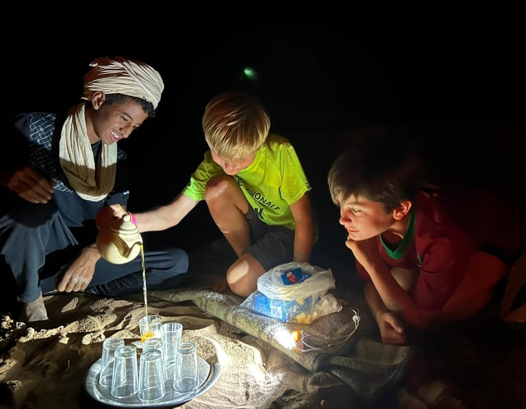 Two boys in the desert being shown how to pour tea Moroccan style
