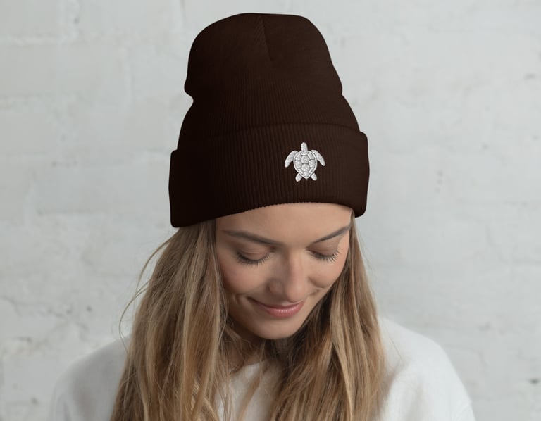 A woman wearing a dark brown cuffed beanie with a white sea turtle embroidery.