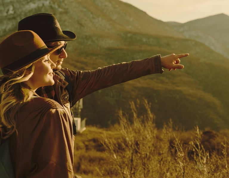 a woman in a hat and a backpack pointing at a mountain