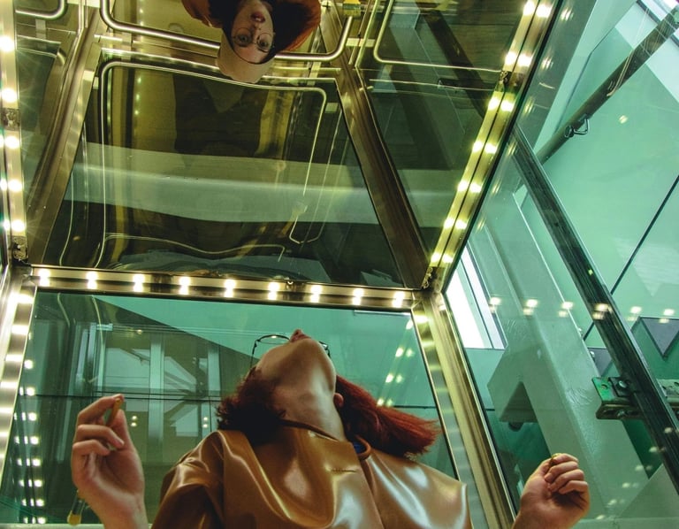 A woman on an elevator looks up at her reflection on the mirrored ceiling panel