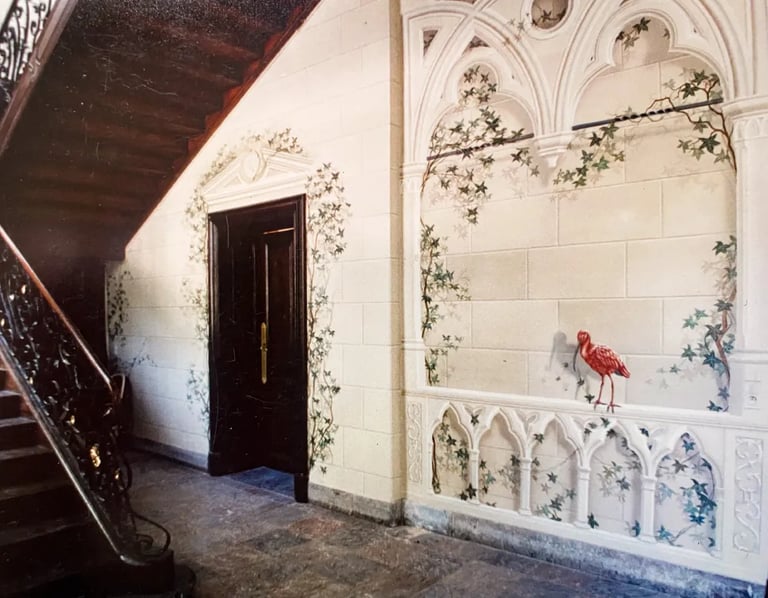 Hallway with wooden staircase and large mural of faux sandstone, ivy, gothic arches, and red bird.