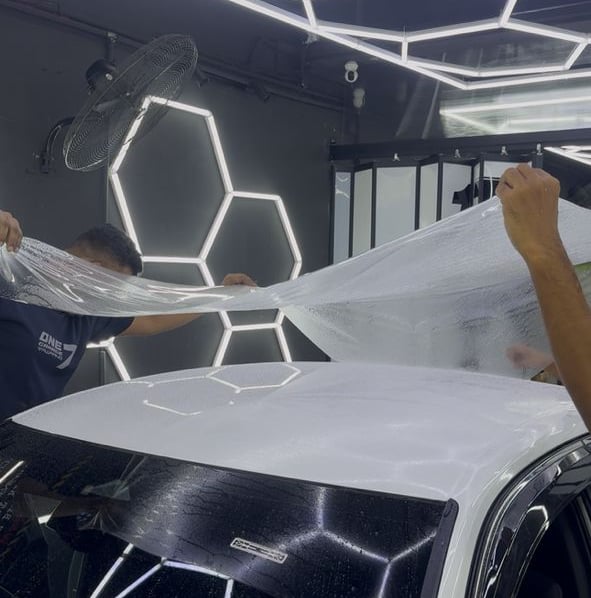 Technicians installing paint protection film on car roof and windshield