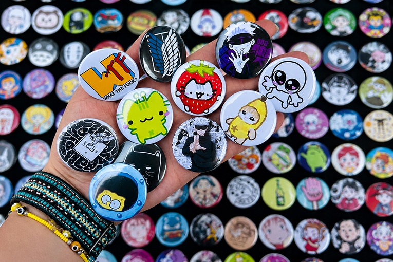 Mano sosteniendo una colección de coloridos botones o pines de anime y dibujos anime cultura geek