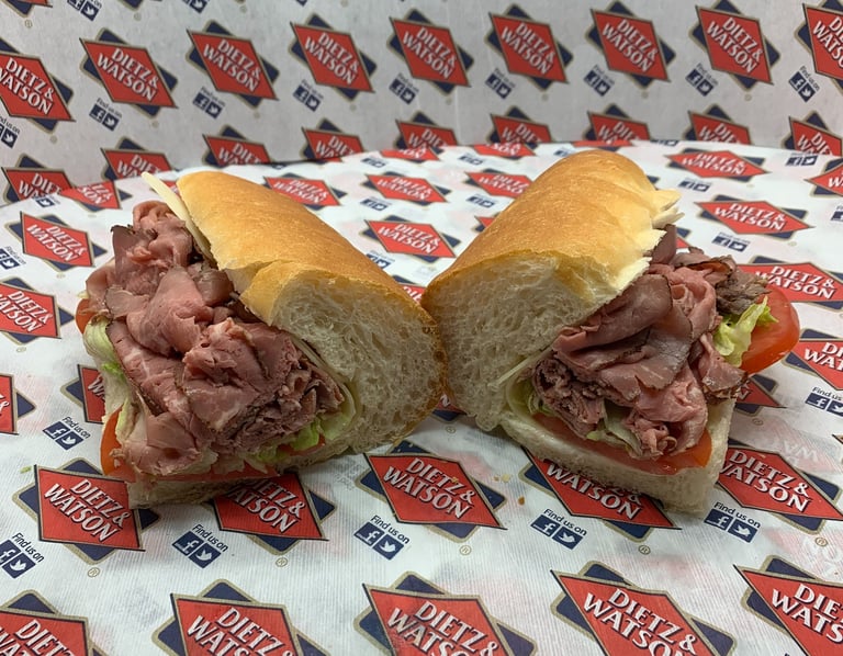 Fresh roast beef deli sub with lettuce and tomato on a long roll atop Dietz and Watson paper.
