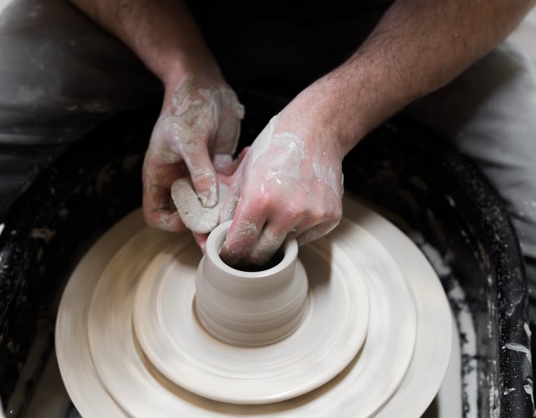 Hands holding a sponge forming a pot on a potter's wheel.