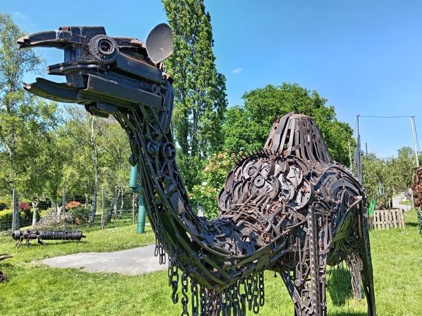 A life-sized camel sculpture made from recycled scrap metal standing in a green park.