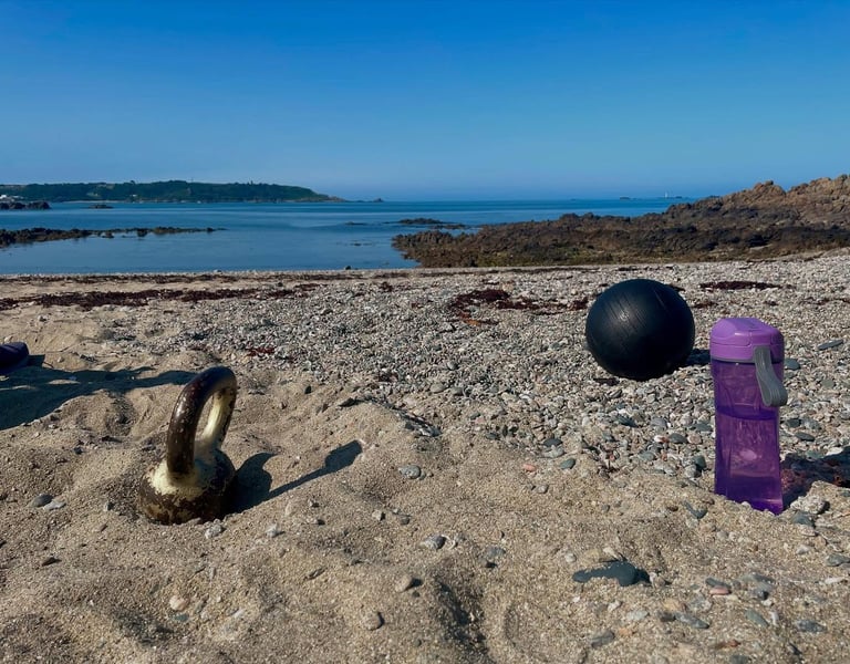 Fitness gear including a kettlebell, medicine ball, and water bottle for a beach workout.