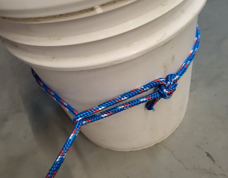 Close up of a running bowline knot tied with blue synthetic rope around a bucket.