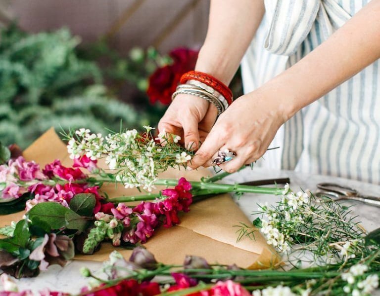 Florista armando un arreglo con flores rosadas y follaje verde.