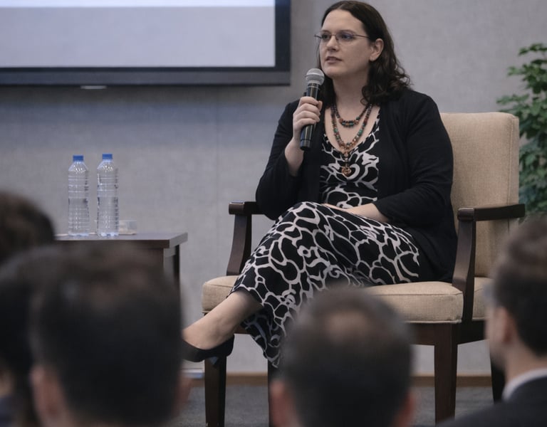 Female speaker holding a microphone while addressing an audience at a business conference panel.