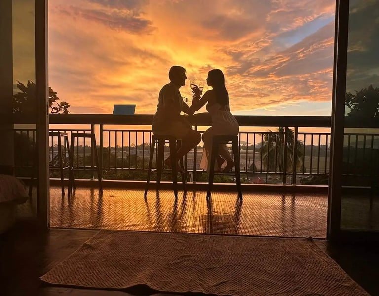 Silhouette of a couple enjoying drinks on a balcony at sunset with a vibrant orange sky.