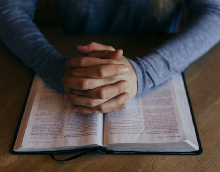 Hands held in prayer resting on a Bible