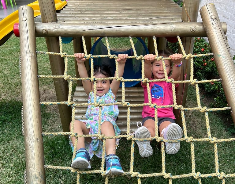 Niñas colgadas de malla en playground de madera en un pasto en Ukelele Jardín Infantil