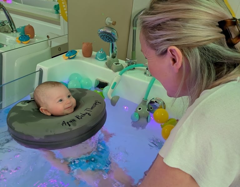 bébé souriant à la praticienne pendant qu'il est dans le bain avec sa bouée de cou