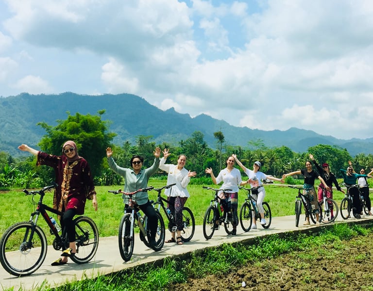 Wisatawan bersepeda santai menyusuri jalan pedesaan dengan pemandangan sawah dan Candi Borobudur di kejauhan
