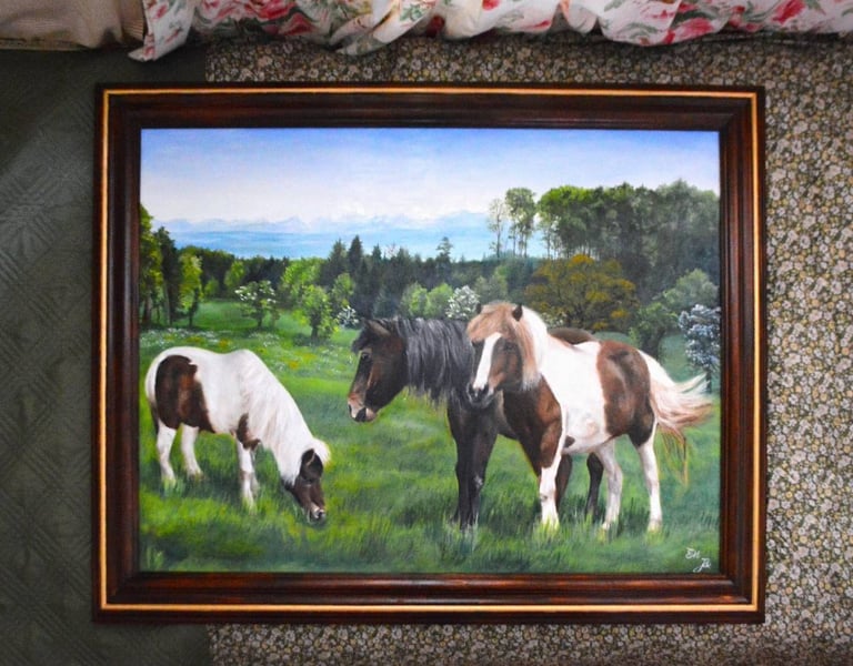 a framed painting of three horses grazing in a field