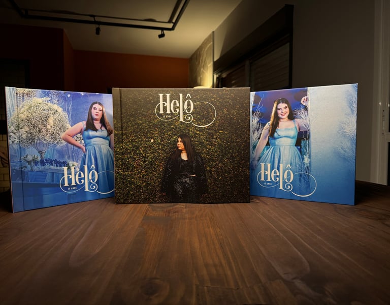 Três álbuns fotográficos de 15 anos com capas personalizadas expostos sobre mesa de madeira.